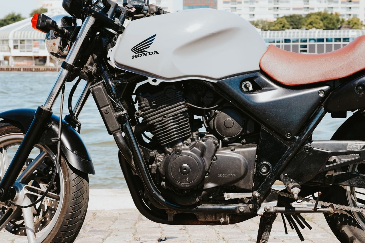 Close-up of a classic Honda motorcycle parked by the waterfront on a sunny day.